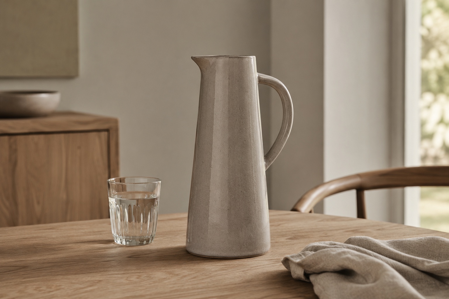 Tall stoneware carafe and water glass on a wooden dining table